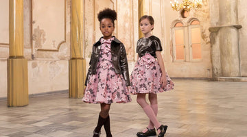 Luxury girls wearing pink floral party dresses with black bolero jackets in an elegant palace interior.