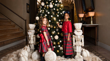 Girls wearing red tartan Christmas outfits by a decorated tree