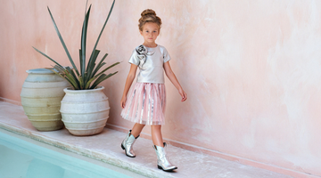 Little girl wearing a stylish ivory top with a pink metallic pleated skirt from Mama Luma, walking gracefully by a poolside — perfect for spring birthdays, tea parties, and outdoor celebrations. Available in sizes 3–12Y.