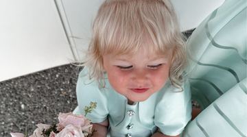 Baby girl in a mint green satin dress holding a bouquet of pink roses, styled with a white hair bow — ideal for weddings, birthdays, and summer celebrations (12–36M)