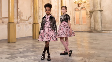 Two girls dressed in Mama Luma’s pink floral couture outfits — one wearing a satin embroidered dress paired with a black cropped jacket, and the other styled in a satin floral skirt and metallic top.
