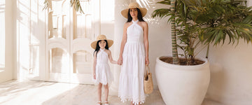 Mother and daughter wearing matching white summer dresses and straw hats, walking through a luxury Mediterranean resort in elegant Mommy & Me vacation outfits perfect for Europe travel.