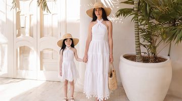 Mother and daughter wearing matching white summer dresses and straw hats, walking through a luxury Mediterranean resort in elegant Mommy & Me vacation outfits perfect for Europe travel.