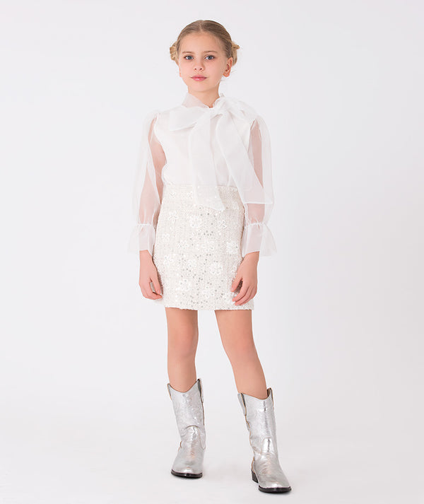 a white sheer blouse with a large bow detail and a sparkling sequin skirt