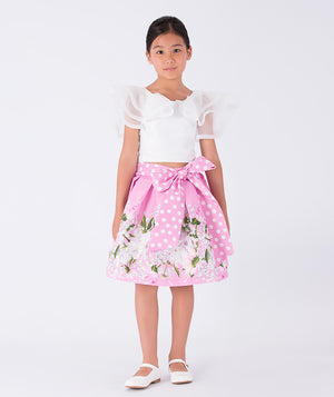 white ruffled blouse and pink floral skirt with a polka dotted bow on the waist