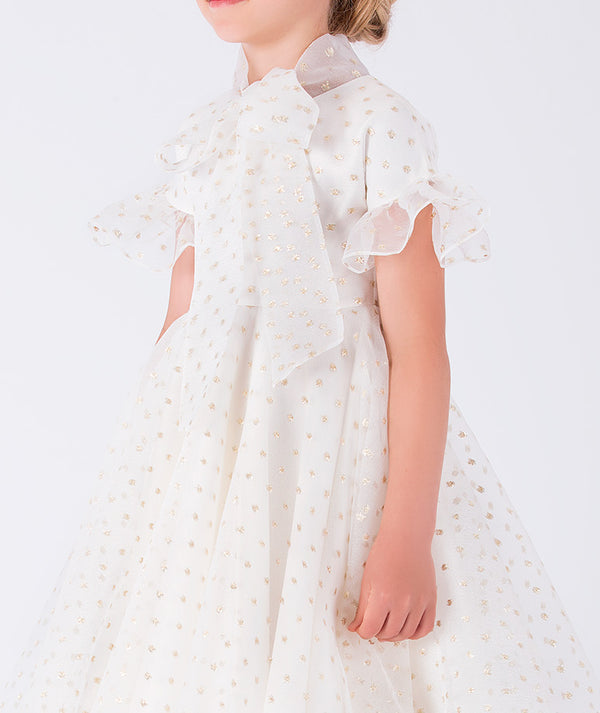 charming organza dress adorned with ruffle details, shimmering golden polka dots, and a statement bow on the front