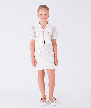 A chic white outfit featuring a delicate jacket and a coordinating skirt, accented with a statement bow