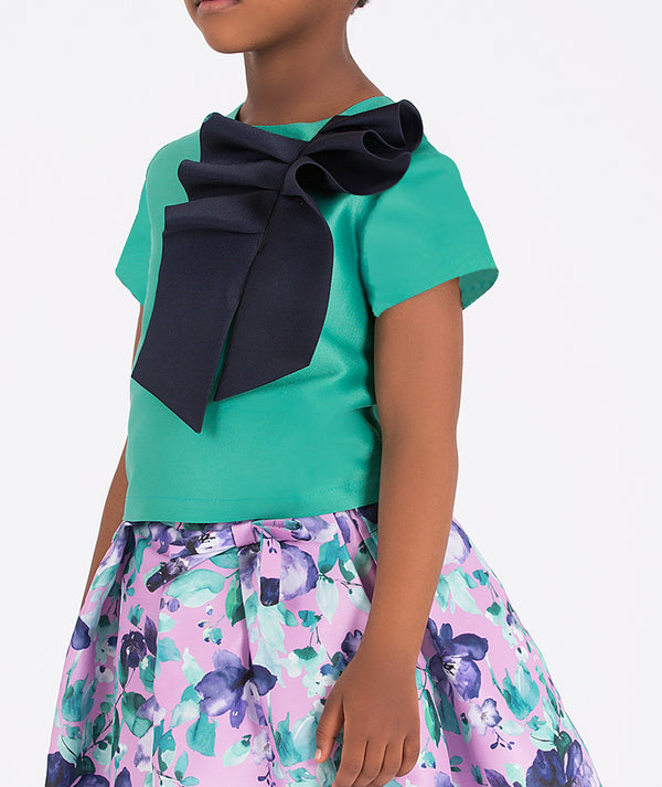 Kids fashion outfit featuring a floral skirt and green top with a navy bow