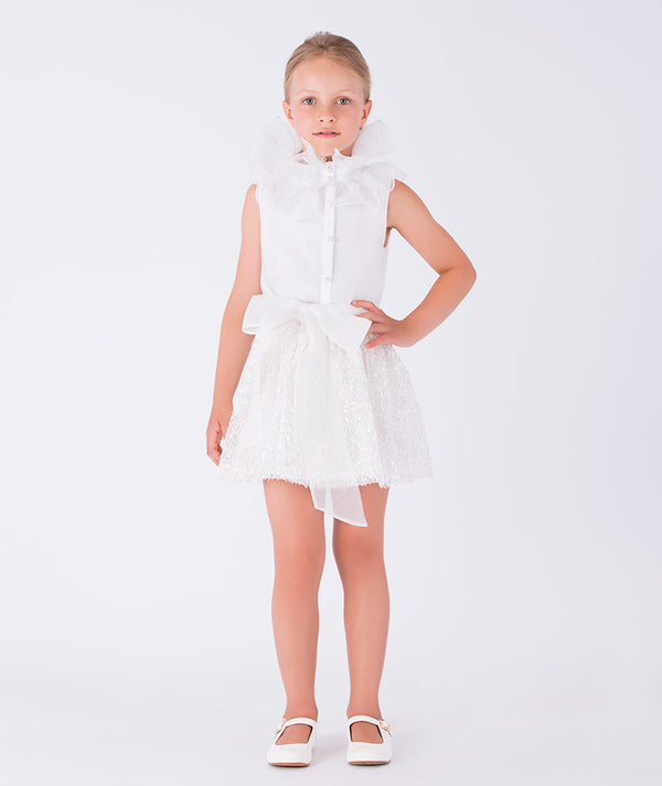 white blouse with organza ruffled neckline and shimmering skirt with an organza bow on the waist