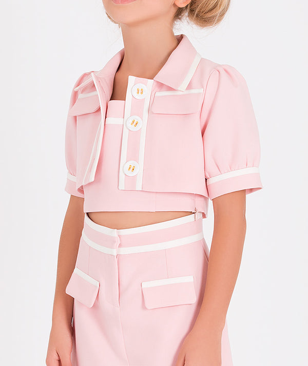 a pink cropped bolero with white trim and large buttons