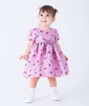 Sweet lilac baby dress adorned with purple orchids and a delicate bow at the waist for a gentle, charming touch.
