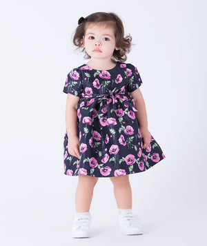 Sweet navy baby dress adorned with purple orchids and a delicate bow at the waist for a gentle, charming touch.