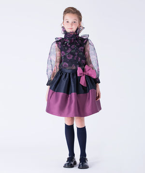 Elegant navy organza blouse with sheer sleeves and ruffled collar, blossoming with purple orchids. Paired with a puff skirt trimmed in purple and a mulberry bow waist detail.