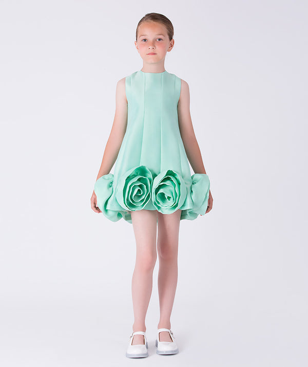 Young girl wearing a light green dress with floral details on a white background