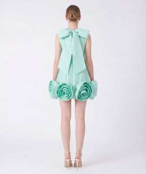 Mint green dress with floral details and a large bow on a white background