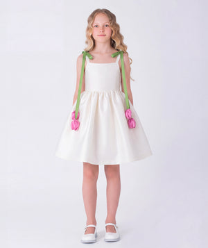 Elegant ivory girls dress featuring soft green shoulder straps with 3D pink tulip accents and a voluminous skirt. A refined special occasion piece designed with delicate structure and timeless charm.