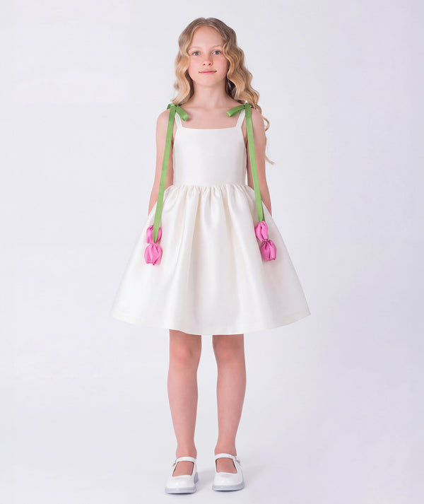 Elegant ivory girls dress featuring soft green shoulder straps with 3D pink tulip accents and a voluminous skirt. A refined special occasion piece designed with delicate structure and timeless charm.