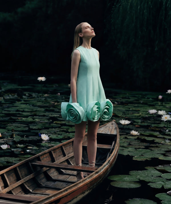 Woman in a floral dress standing on a boat in a pond with lily pads.