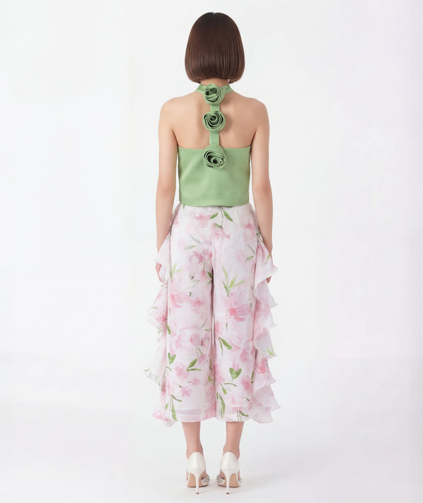 Woman wearing a green flower detail top with floral patterns and white pants on a white background
