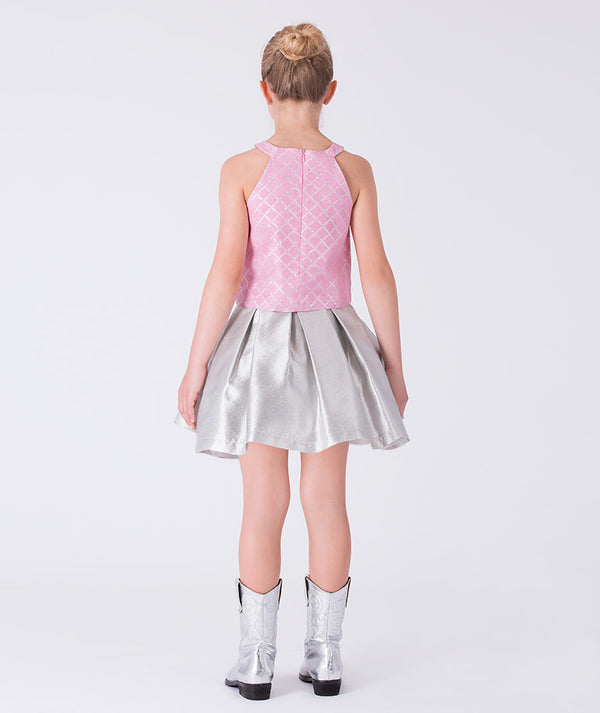 7 years old wearing a pink quilted top and silver skirt with matching shoes on a white background