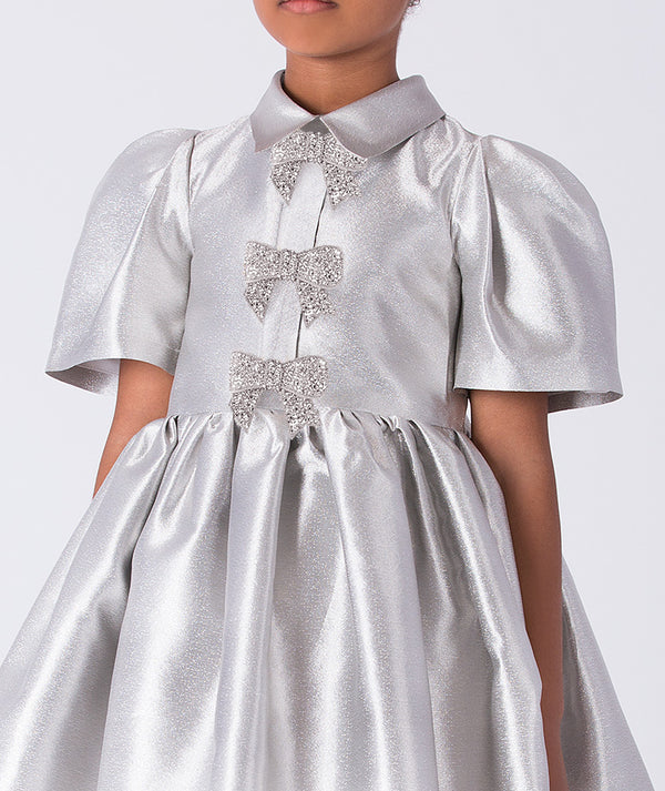 Silver dress with bow details on a plain background