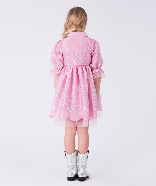 8 year old girl wearing a pink dress with a pattern, standing against a white background