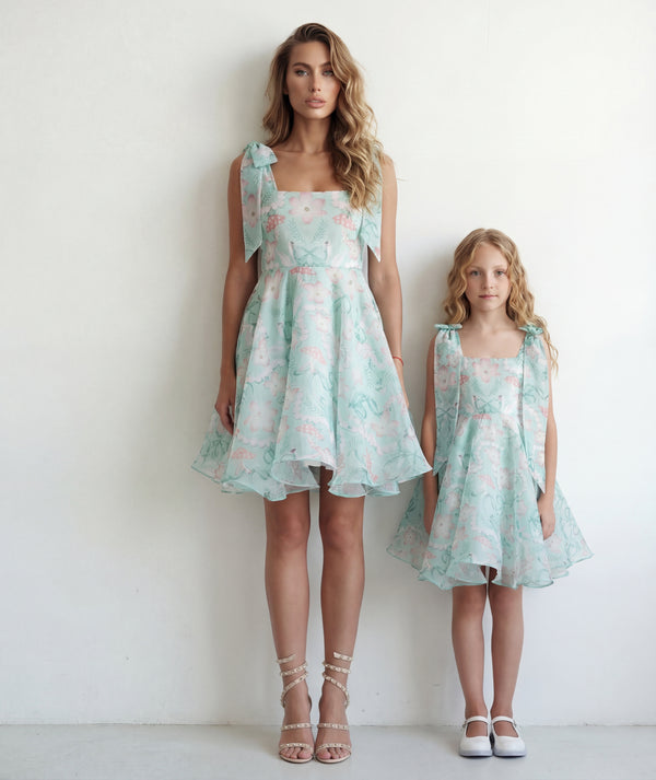 a mom and her daughter wearing matching floral dresses against a white background