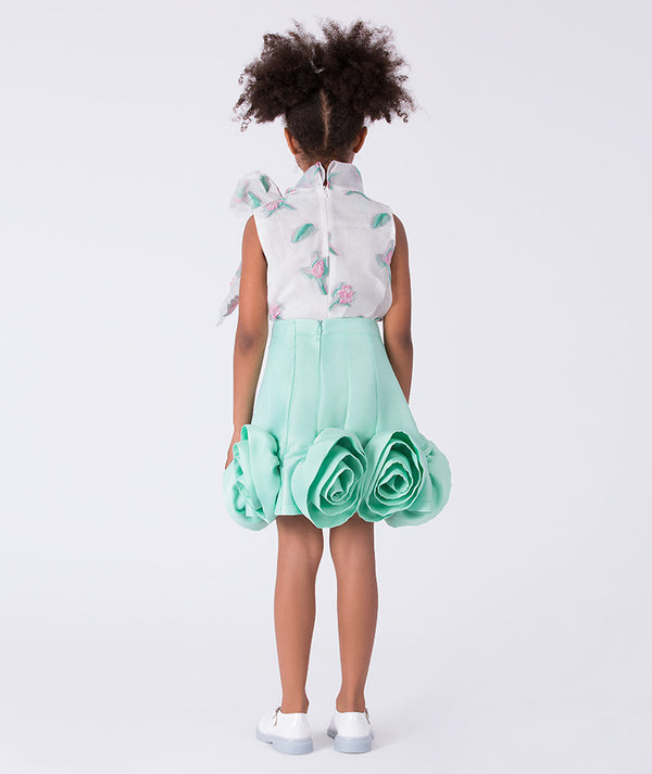 Young girl wearing a floral top and mint green skirt on a white background