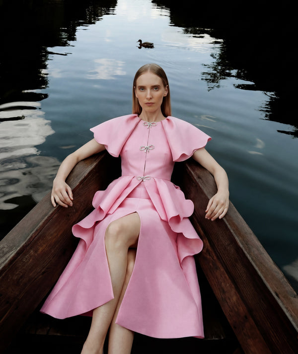 Woman in a pink dress sitting in a boat on a body of water.