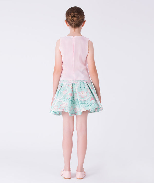 Young girl wearing a light pink top and floral skirt on a white background
