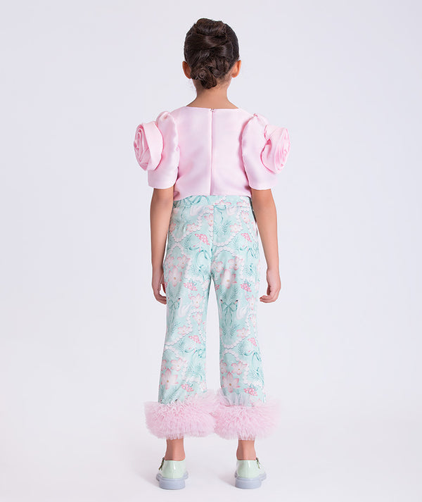 Child wearing a pink top with puff sleeves and floral-patterned pants on a white background