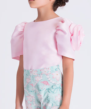 6 year old wearing a pink top with puffed sleeves and floral-patterned pants on a white background