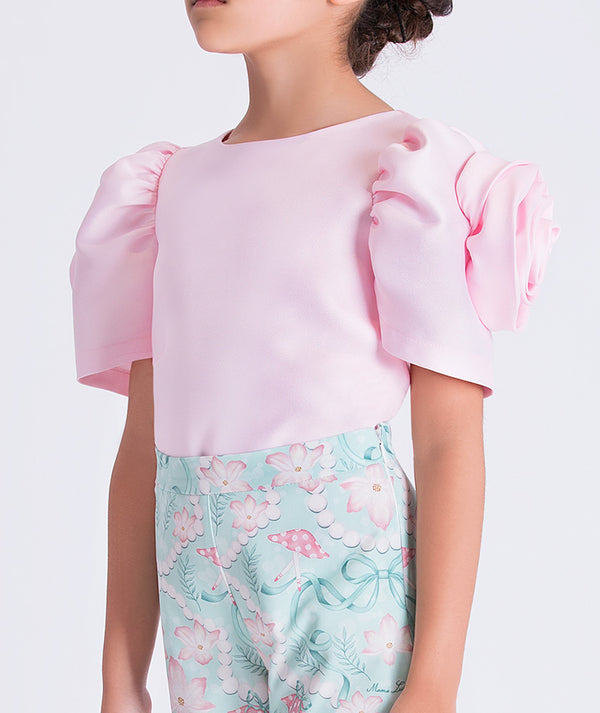 6 year old wearing a pink top with puffed sleeves and floral-patterned pants on a white background