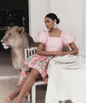 Woman in a pink dress sitting at a table with a lion beside her