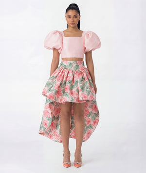 Woman wearing a pink top with puff sleeves and a floral skirt on a white background