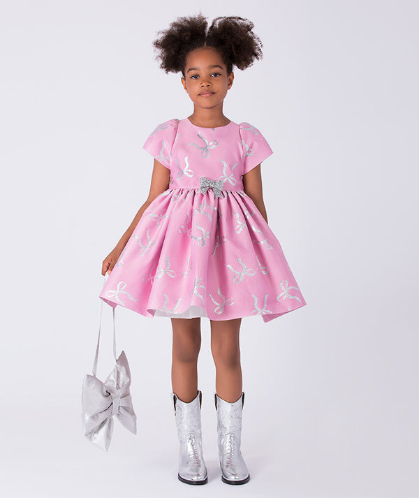 6 YEARS OLD girl wearing a pink dress with white patterns, holding a matching bag, on a white background