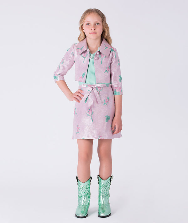 Girl wearing a pink floral dress with a green belt and green boots on a white background