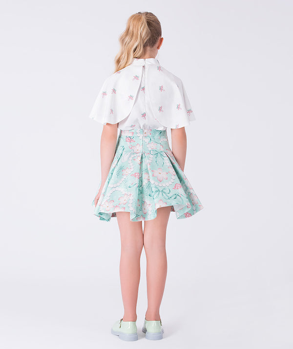 7 years old girl wearing a white blouse with floral sleeves and a light blue floral skirt on a white background