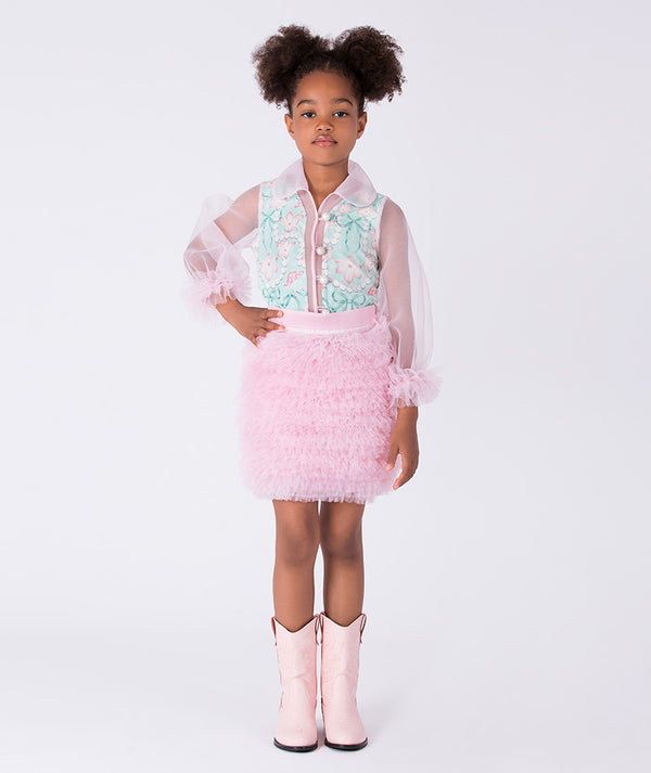 Young girl wearing a light blue top, pink skirt, and pink boots on a white background