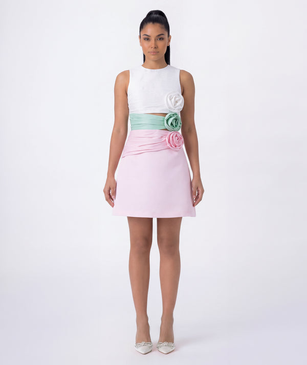 Woman wearing a white top and pink skirt with floral details on a white background