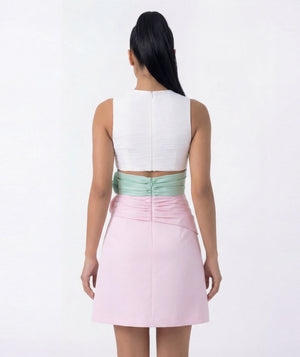 Woman wearing a white top and pink skirt with green waistband on a white background