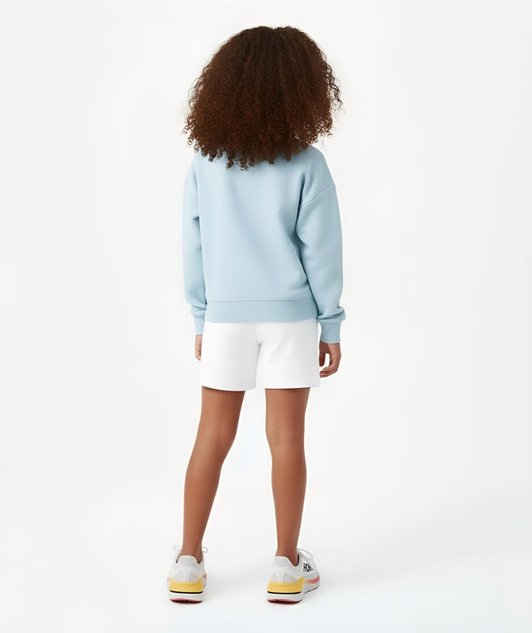 Girl seen from the back wearing a light blue sweatshirt and white shorts, styled for everyday athleisure, school days, and active play, available in sizes 3–14