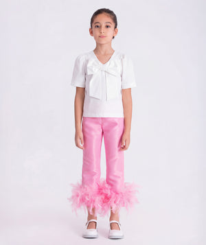 6 years old girl wearing a white blouse and pink pants with ruffles on a white background