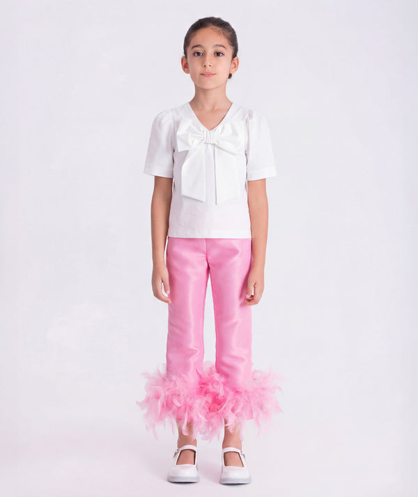 6 years old girl wearing a white blouse and pink pants with ruffles on a white background