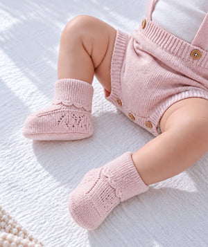 Pink knitted baby booties in a product detail photograph.