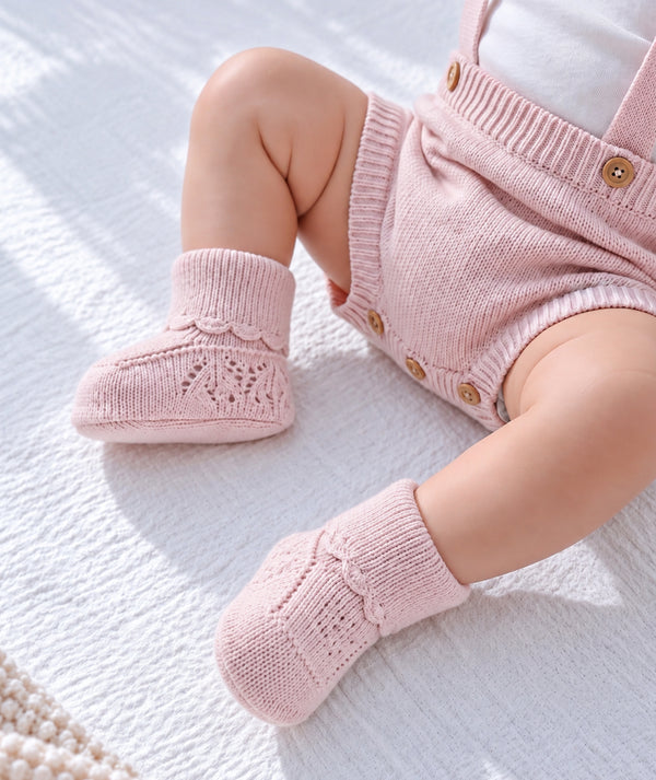 Pink knitted baby booties in a product detail photograph.
