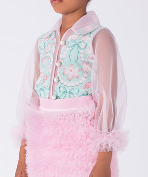 toddler wearing a floral top with a sheer pink jacket and pink skirt on a white background