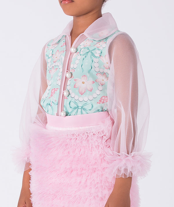 toddler wearing a floral top with a sheer pink jacket and pink skirt on a white background