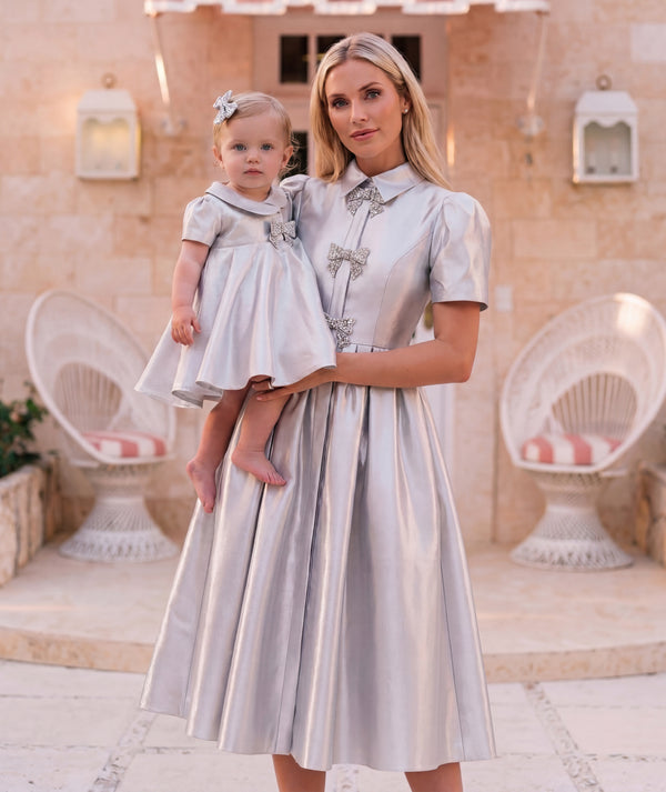 Editorial view of Crystal Bow Silver Baby Dress in silver structured fabric for babies 12 to 36 months, featuring fabric texture and color