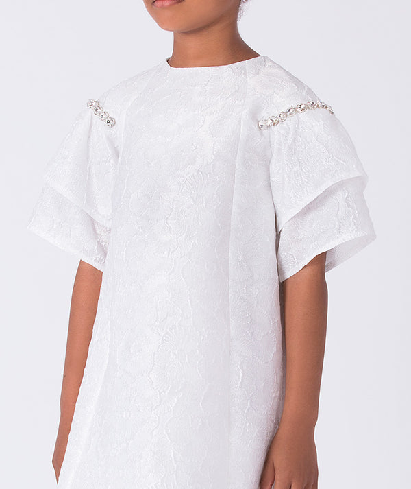 Close-up of crystal embellishments at the shoulders of a white girls dress, highlighting refined craftsmanship and subtle sparkle